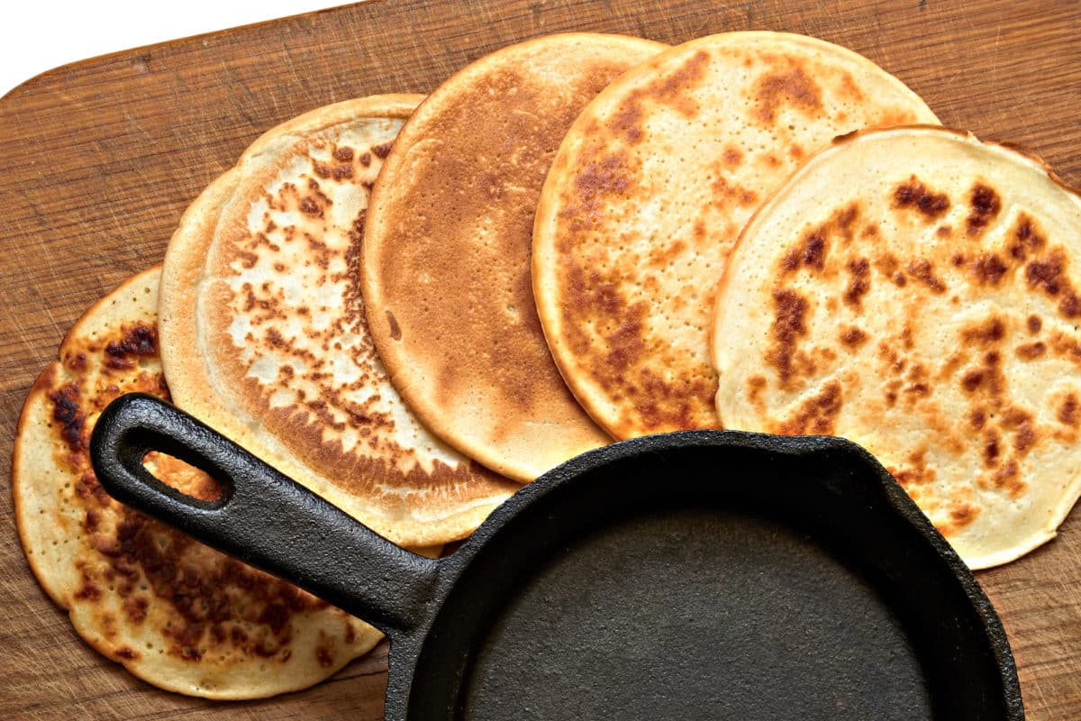 A stack of four pancakes in a cast iron skillet on a wooden board.