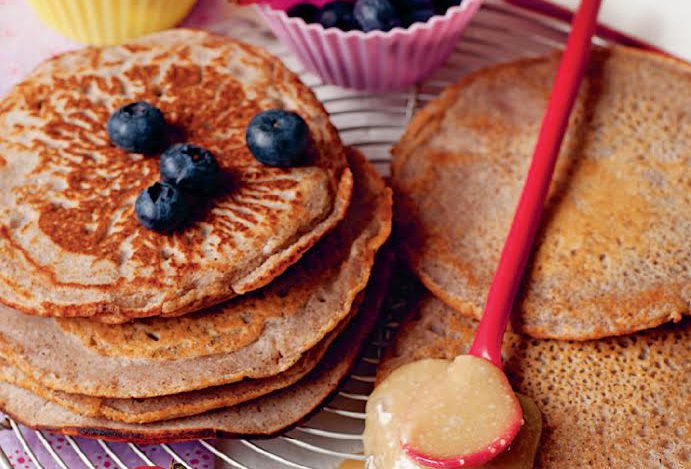 Stack of golden-brown pancrepes topped with fresh blueberries and a side of sauce.